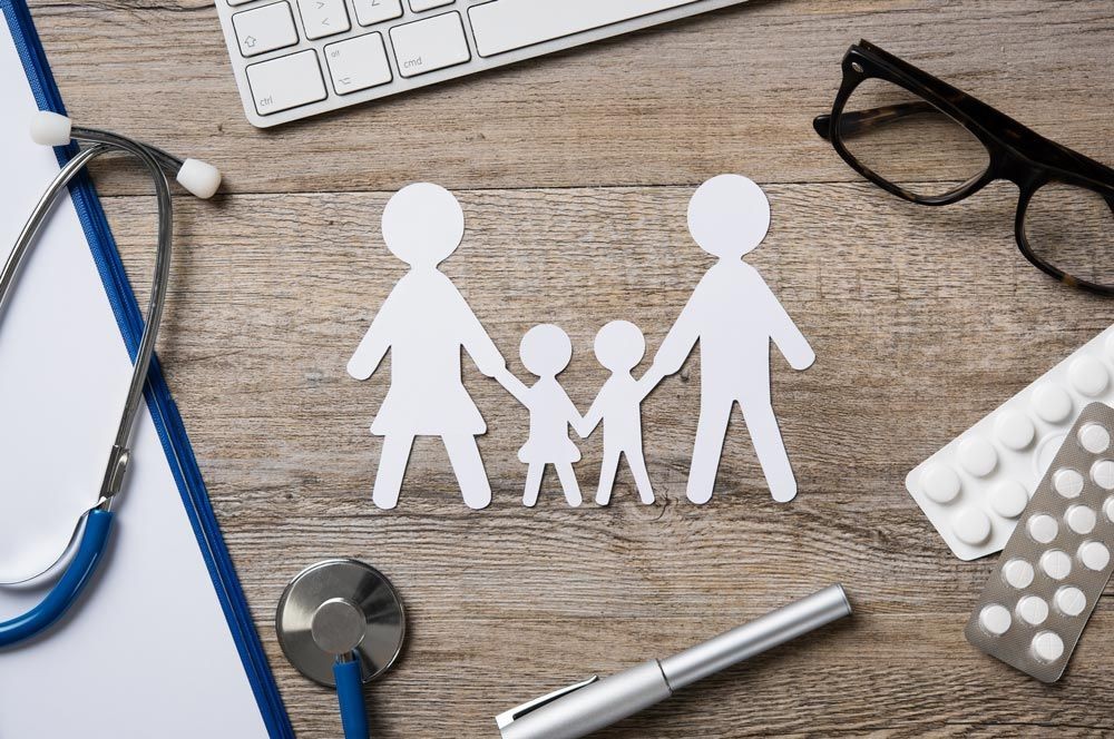 Paper cut-out family with medical items, keyboard, and glasses on a wooden table.