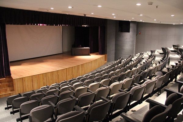 Empty auditorium with rows of seats facing a stage and a large screen.